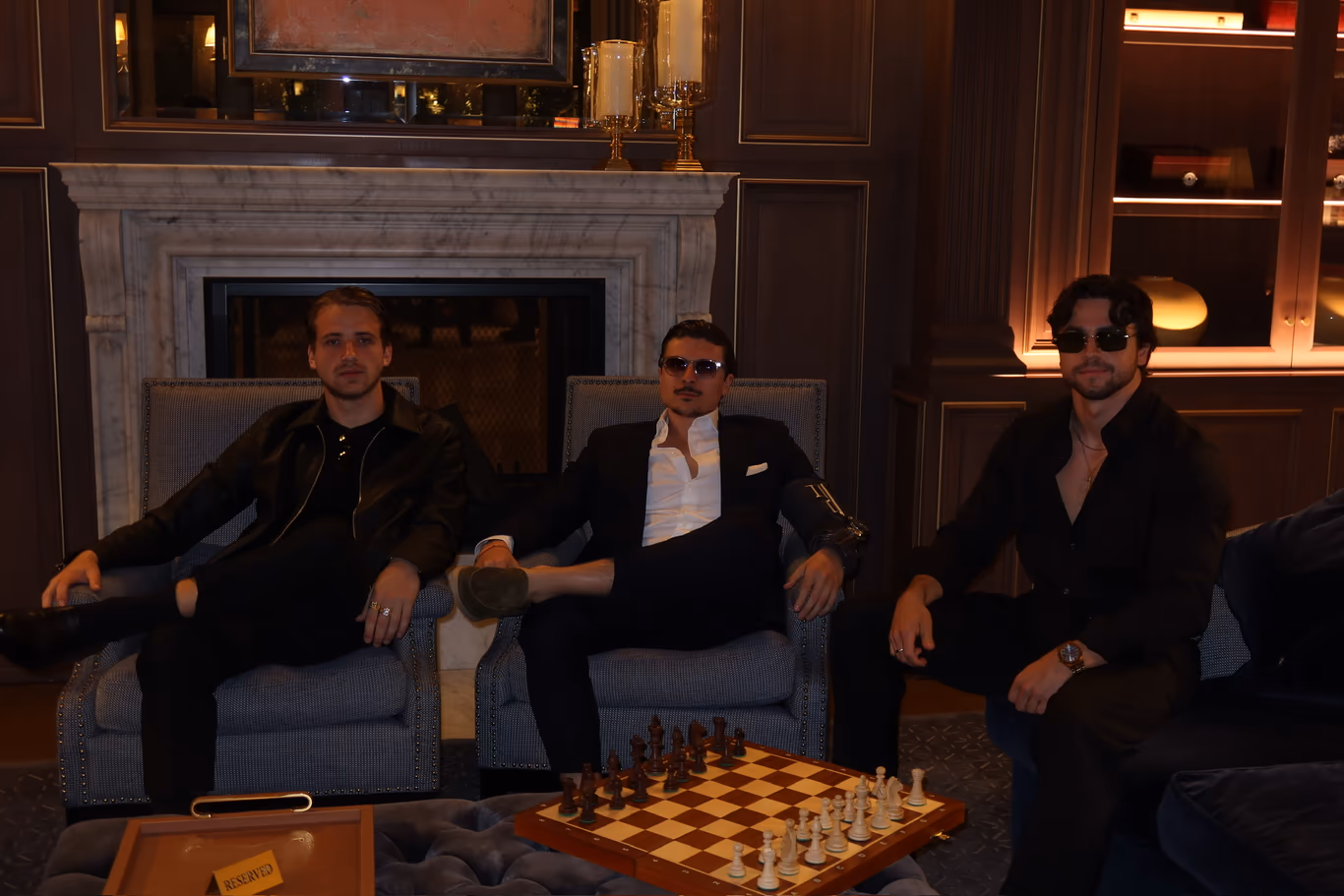 Three founders seated around a chessboard in a fireside lounge