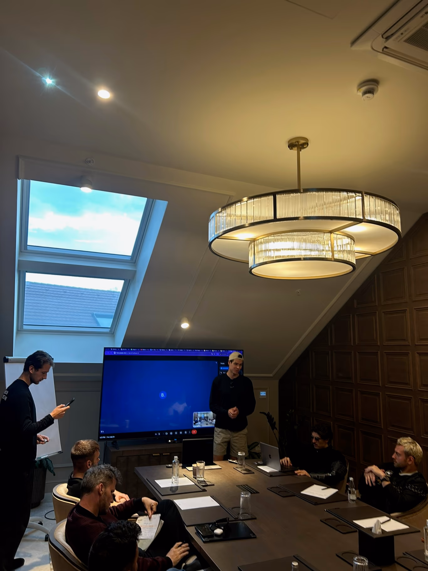 A founder presenting to seated peers around a conference table — accountability in front of the room