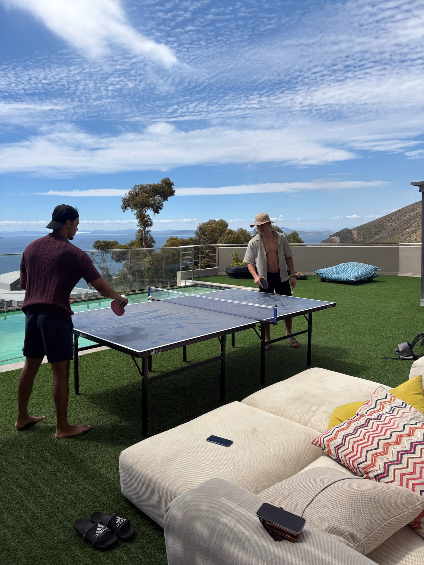 Two founders playing table tennis on a villa terrace overlooking the sea