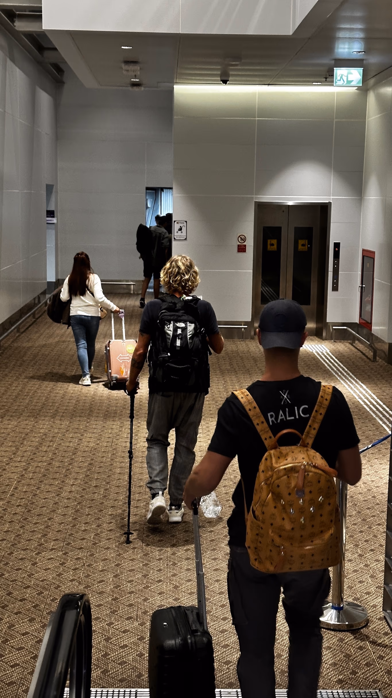 Helix trips — wheels down Founders wheeling rolling suitcases down a carpeted terminal corridor toward an elevator on a Helix trip