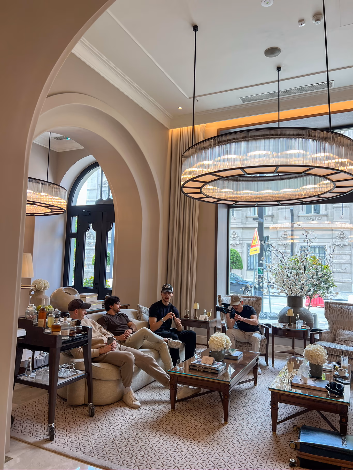 Four founders seated on cream sofas under a large round chandelier in a grand hotel lounge with arched windows