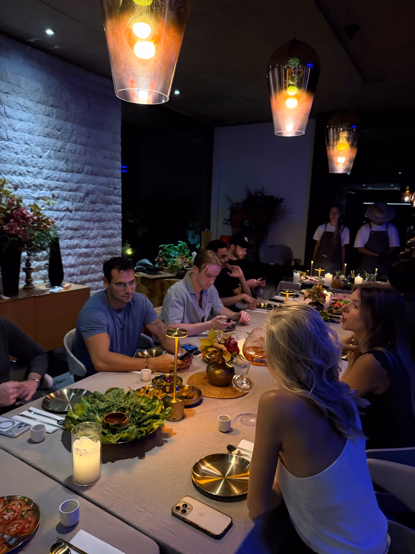 Founders around a long candlelit table at an evening dinner, shared dishes down the middle and staff serving in the background — a mastermind dinner in full swing