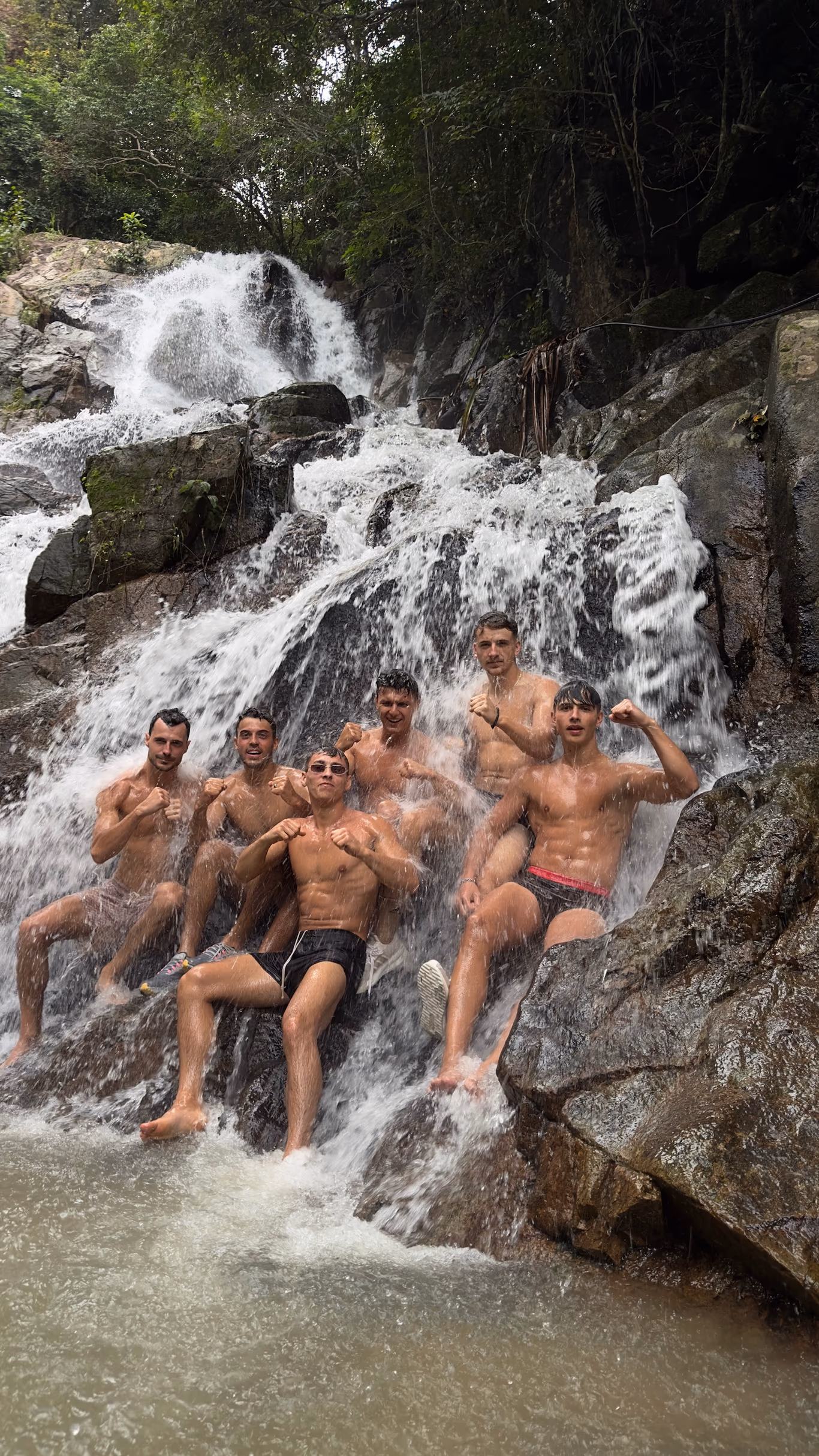 Founder travel group — off the itinerary A founder travel group posing together in swim trunks under a cascading waterfall on a Helix trip — off the itinerary